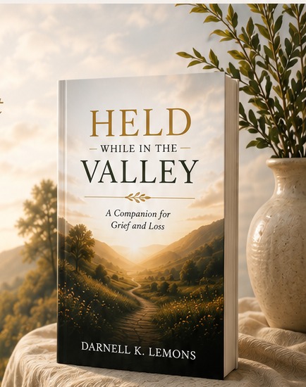 Held While in the Valley paperback book resting on a table beside a vase and plant